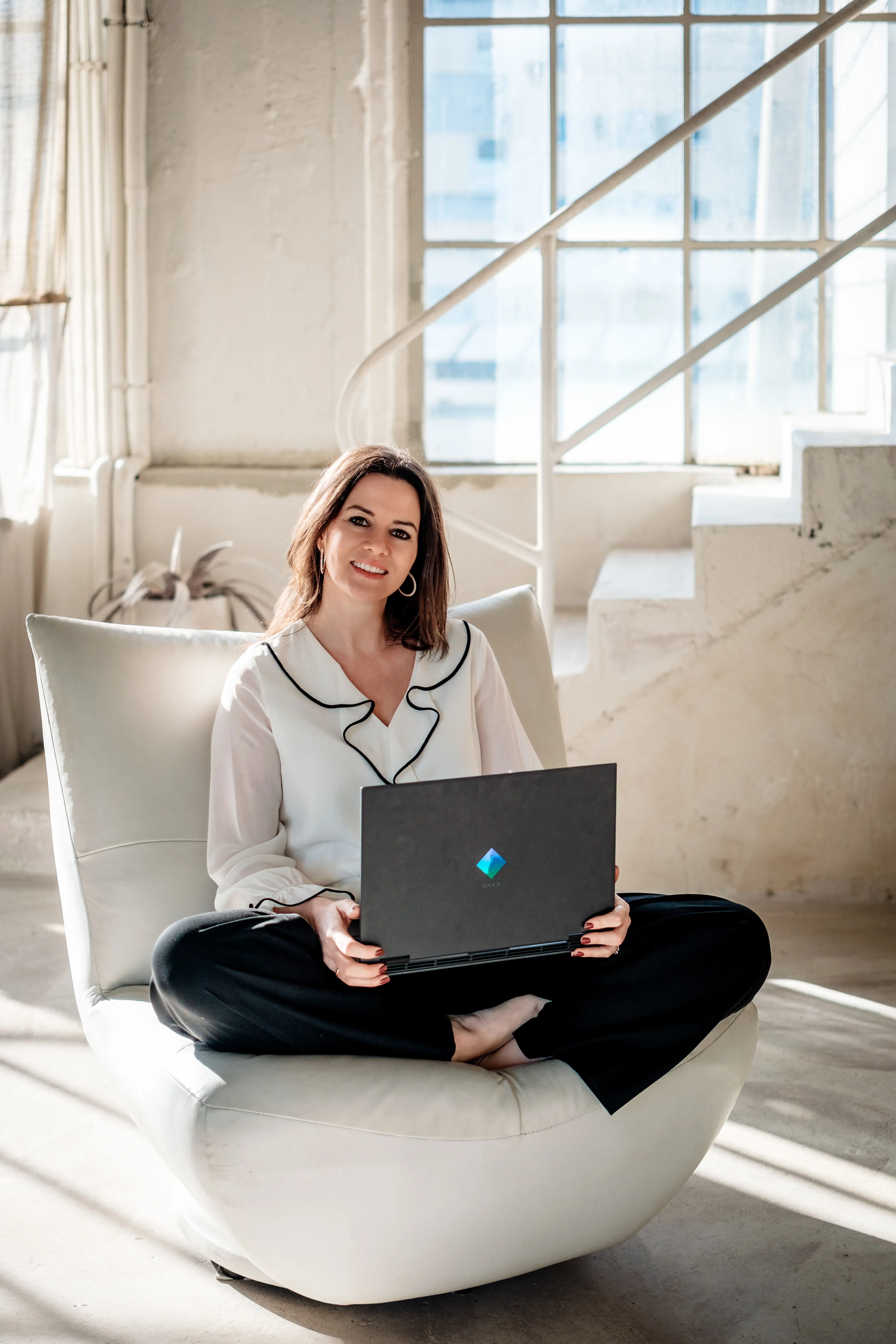 Sarah-Yasmin Hennessen sitzt mit einem Laptop in einem hellen Sessel.